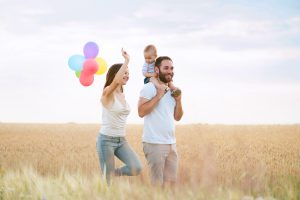 Happy family having fun in wheat field. Mother, father and child playing with balloons