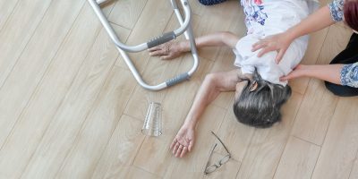 Woman lying on floor after falling, beside a walking aid and glasses